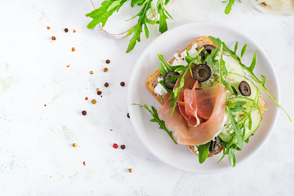 Sandwich with prosciutto, cucumber, black olives, arugula and feta cheese